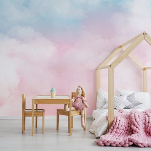 May include: A pink and blue watercolor cloud wallpaper with a wooden house bed frame, a pink knitted blanket, and a small wooden table and chairs.
