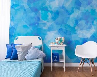 Puede incluir: Una cama blanca con ropa de cama y almohadas azules en una habitación con un papel tapiz de patrón geométrico azul. Una mesita de noche blanca con un cuenco decorativo de bolas blancas y una pequeña figurita dorada se encuentra junto a la cama. Una silla blanca con patas de madera se encuentra en la esquina de la habitación.