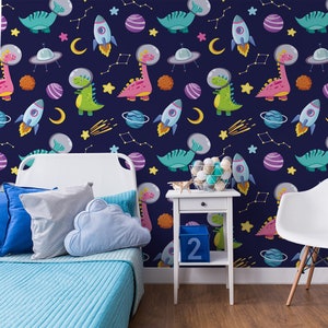 May include: A blue and white wallpaper with a repeating pattern of dinosaurs, rockets, stars, and planets. The wallpaper is in a child's bedroom with a white bed, blue pillows, and a white chair.