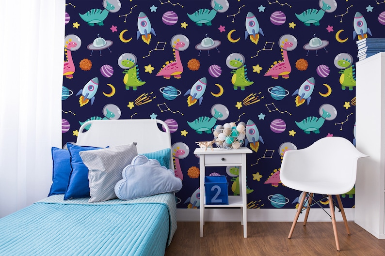 May include: A blue and white wallpaper with a repeating pattern of dinosaurs, rockets, stars, and planets. The wallpaper is in a child's bedroom with a white bed, blue pillows, and a white chair.