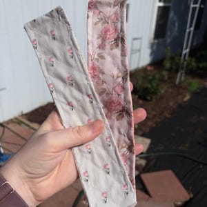 May include: Two long, rectangular fabric strips featuring quilted diamond stitching. One strip has a light gray background with small pink rosebuds, while the other features a dense, larger-scale pink and green floral rose pattern on a light pink base.