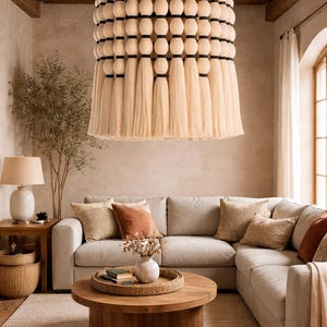 May include: A large, beige chandelier with a tiered design hangs above a living room. The chandelier features wooden beads, black accents, and long, flowing tassels. The room includes a sectional sofa, coffee table, and neutral color palette.