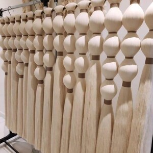 以下が含まれることがあります： 金属製の棒から吊り下げられた、オフホワイトの装飾用タッセル。各タッセルは、一連の丸みを帯びた積み重ねられた要素と、長く流れるフリンジが特徴です。タッセルは茶色のバンドで結ばれ、質感のあるエレガントなディスプレイを作り出しています。