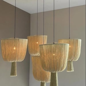 Op de afbeelding: Vijf hanglampen met beige geweven kappen en bijpassende kwasten. De lampen hangen aan zwarte snoeren, wat een warme sfeer creëert. De kappen hebben een textuur en natuurlijke uitstraling.