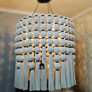 May include: A white macrame chandelier with black accents and tassels. The chandelier is made of a series of woven balls with a black band around each ball.