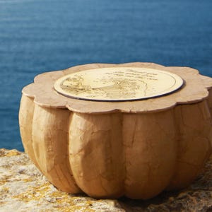 Handmade BLUE SOUL biodegradable water burial urn for ashes, crafted from natural paper mache with a wooden lid, shown beside the sea