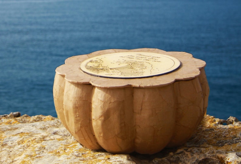 Handmade BLUE SOUL biodegradable water burial urn for ashes, crafted from natural paper mache with a wooden lid, shown beside the sea