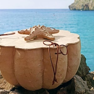 SOUL SEA biodegradable water burial urn handmade from paper mache with a starfish sea life symbol on the wooden lid, photographed beside the Mediterranean sea