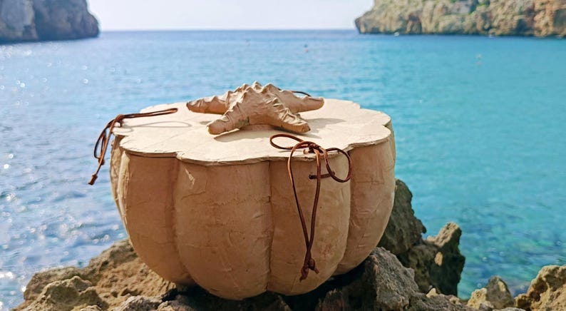 SOUL SEA biodegradable water burial urn handmade from paper mache with a starfish sea life symbol on the wooden lid, photographed beside the Mediterranean sea