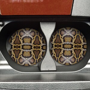 Peut inclure: Deux dessous-de-verre ronds à motif de peau de serpent brun et beige dans un porte-gobelet de voiture.