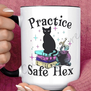 Puede incluir: Taza de cerámica blanca con asa negra. La taza tiene un gato negro sentado sobre una pila de libros con un caldero a su lado. El texto en la taza dice "Practice Safe Hex".