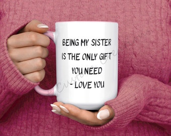 May include: White ceramic mug with a pink rim and handle. The mug has black text that reads "Being my sister is the only gift you need - Love you".