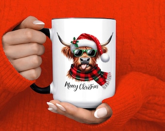 May include: White ceramic mug with a black handle and rim, featuring a cartoon Highland cow wearing a Santa hat, sunglasses, and a plaid scarf. The mug has the text "Moocy Christmas".