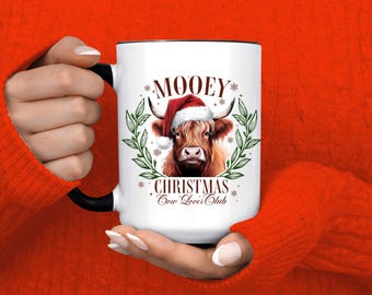 May include: White ceramic mug with a black handle and rim. The mug features a festive design with a Highland cow wearing a Santa hat, surrounded by greenery and snowflakes. Text on the mug reads "MOOEY CHRISTMAS Cow Lover's Club."