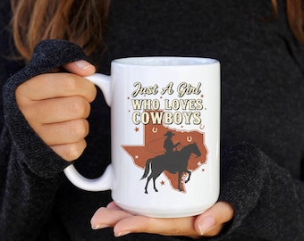 May include: White ceramic mug with the text "Just A Girl Who Loves Cowboys" and a silhouette of a cowboy on a horse within a Texas outline. The mug has a large handle.