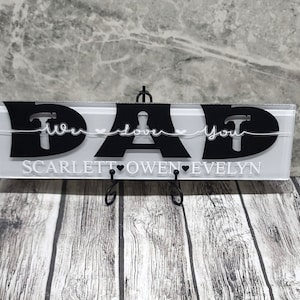 May include: White acrylic sign with black lettering that reads "DAD We love you" with a hammer graphic on each side. The names Scarlett, Owen, and Evelyn are written below the main text with a heart between each name.
