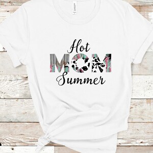 May include: White t-shirt with the text "Hot Mom Summer" in black lettering. The word "Mom" is in colorful, patterned letters.