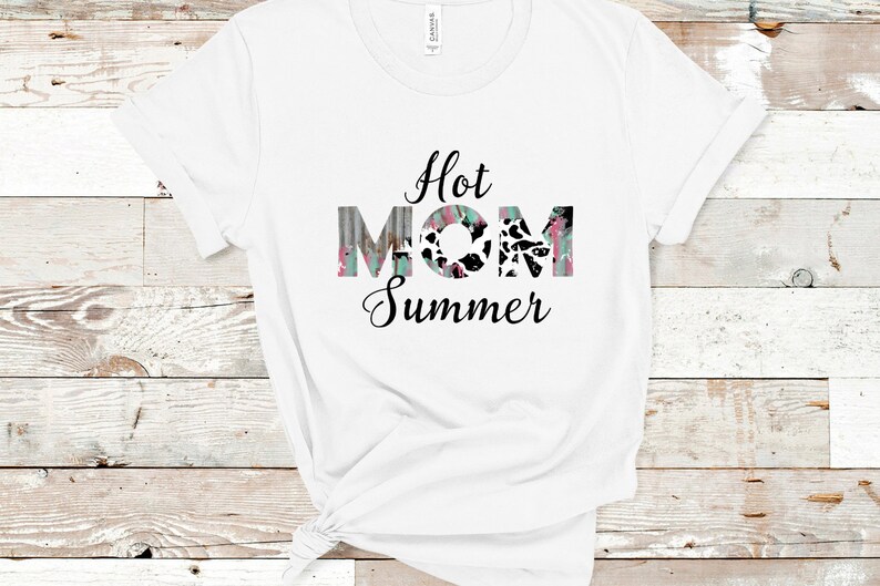 May include: White t-shirt with the text "Hot Mom Summer" in black lettering. The word "Mom" is in colorful, patterned letters.