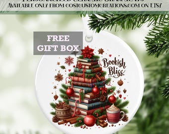 May include: A white ceramic Christmas bauble featuring a stack of books arranged as a Christmas tree. The books are adorned with red and green baubles and cinnamon sticks. The bauble has the text "Bookish Bliss" on it.