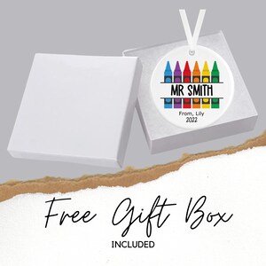 May include: A white ceramic bauble with a rainbow of crayons around the edge. The bauble says "MR SMITH" in black text and "From, Lily 2022" in smaller black text. The bauble comes in a white gift box.