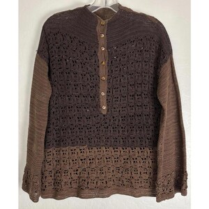 Könnte beinhalten: Ein brauner Häkelpullover mit langen Ärmeln und einem Knopfleisten-Ausschnitt. Der Pullover hat ein strukturiertes, offenes Design und ist aus zwei Brauntönen gefertigt. Die Ärmel sind einfarbig braun.