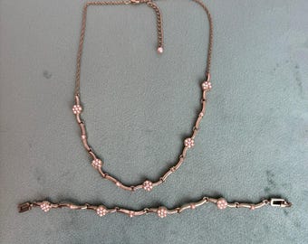 Conjunto de colar e pulseira com pingente de flor em tom de ouro rosa e pérolas artificiais rosa com cristais.