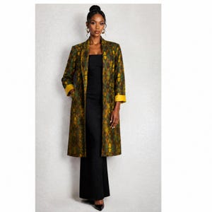 May include: A long-sleeved, knee-length coat featuring a geometric pattern in shades of olive green, mustard yellow, and dark brown. The coat has a solid mustard yellow lining visible at the cuffs and is worn over a simple black dress.
