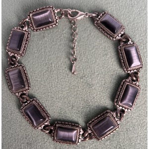 May include: Silver-toned bracelet featuring rectangular, gray-blue stones. Each stone is set within a decorative frame, connected by a chain. The bracelet has an adjustable length and a lobster clasp closure.
