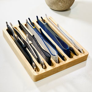 May include: A wooden watch band organizer with eight slots to hold different watch bands. The organizer is made of light brown wood and has a natural finish. The watch bands are a variety of colors, including black, gray, blue, and white.