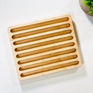 May include: A wooden tray with eight long, narrow slots. The tray is made of light wood and has a smooth, polished finish.