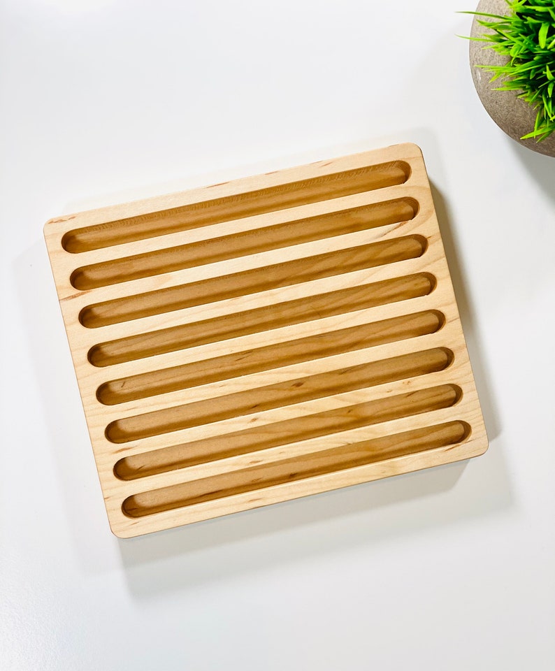 May include: A wooden tray with eight long, narrow slots. The tray is made of light wood and has a smooth, polished finish.