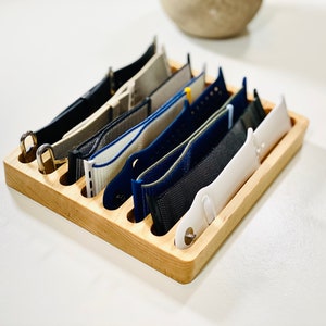 May include: A wooden watch band organizer with eight slots to hold different colored watch bands.