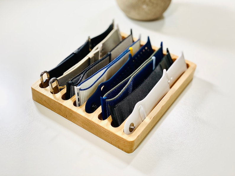 May include: A wooden watch band organizer with eight slots to hold different colored watch bands.