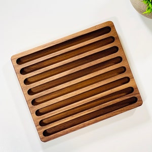 May include: A wooden tray with 10 slots for storing items. The tray is made of dark brown wood and has a rectangular shape.