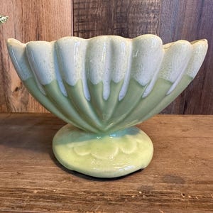 May include: A light green ceramic bowl with a scalloped rim and a pedestal base. The bowl has a glossy finish with white accents on the rim. The base is a lighter shade of green. The bowl is likely vintage or retro.
