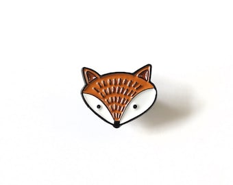 May include: A brown and white enamel pin featuring a cartoon fox face.