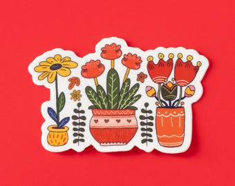 May include: A sticker featuring three potted plants with colorful flowers. The sticker includes a yellow sunflower, red tulips, and red flowers with yellow centers. The pots are orange and red with decorative details, set against a red background.