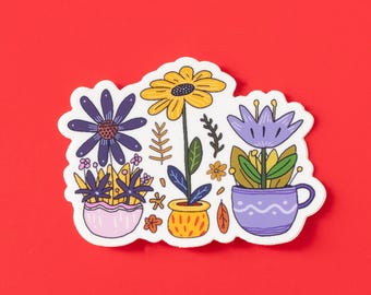 May include: A colorful sticker featuring illustrated flowers in pots. The sticker includes a large yellow daisy, a purple aster, and a purple flower in a teacup. The sticker is on a red background. The sticker is a floral design.