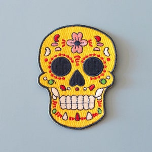 Peut inclure: Patch brodé de sucre jaune avec des yeux noirs, des dents rouges et blanches et un motif de fleur rose.