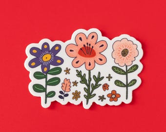 May include: A sticker featuring three stylized flowers in shades of purple, peach, and pink, with green stems and leaves. Additional small floral and leaf elements are scattered around the flowers. The sticker has a white border and is set against a red background.