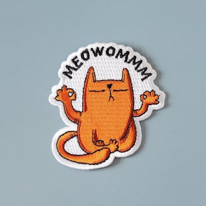 May include: Orange cat meditating with the text "MEOWOMMM" above it. The cat is sitting in a yoga pose with its eyes closed and its paws in a relaxed position. The cat is embroidered on a white background.