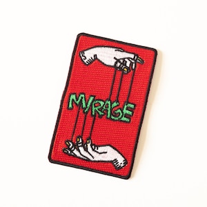 Peut inclure: Un écusson rectangulaire rouge avec une bordure noire. L'écusson présente deux mains blanches avec des accents jaunes, reliées par des fils au mot vert "MIRAGE". L'écusson est probablement un accessoire à repasser ou à coudre.