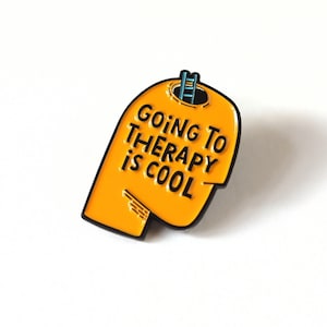 Puede incluir: Pin de esmalte amarillo con forma de cabeza con una escalera que sube a la parte superior de la cabeza. El pin dice "Ir a terapia es genial."