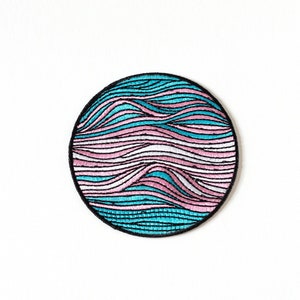 May include: A circular embroidered patch with a black outline. The design showcases horizontal, undulating lines in turquoise, pale pink, and white. The patch is designed for application on clothing or accessories.