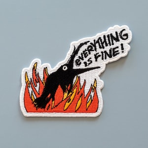 May include: An embroidered patch featuring a black bird engulfed in flames, with the text "EVERYTHING IS FINE!" above it.
