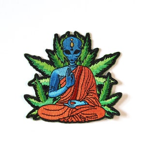 May include: An embroidered patch depicting a blue alien meditating in a lotus position, wearing an orange robe, surrounded by green marijuana leaves.