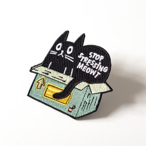 Può includere: Toppa ricamata nera da stirare con un gatto seduto in una scatola con il testo "Stop stressing meowt".