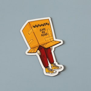 May include: A sticker of a person wearing a cardboard box on their head. The box has the words "Introverting Leave Me Alone" written on it. The person is wearing red pants and yellow shoes.