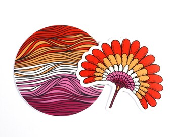 May include: A circular sticker featuring wavy horizontal lines in shades of red, orange, white, pink, and dark magenta, paired with a fan-shaped sticker displaying layered, petal-like segments in the same vibrant color palette.
