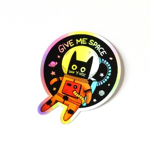 May include: A black cat wearing an orange spacesuit with the text "Give Me Space" in a rainbow holographic circle.